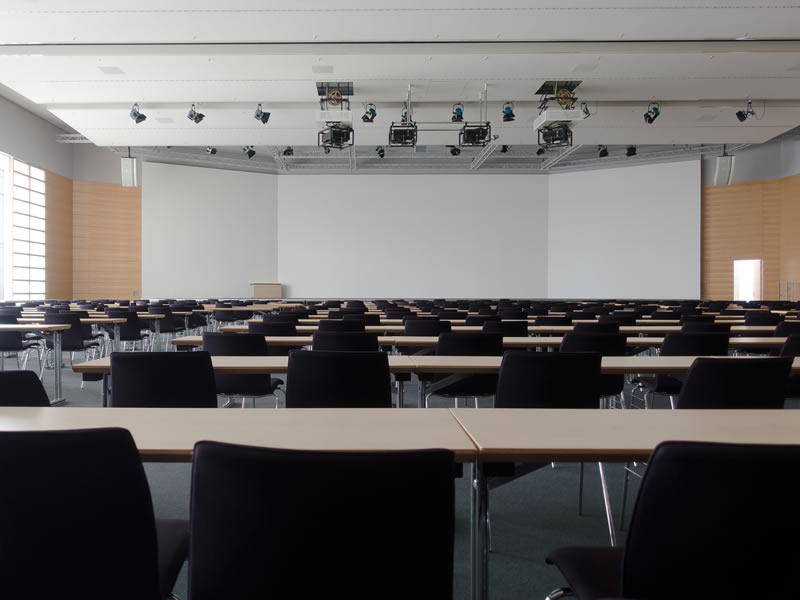 Schulungsraum mit Stuhlreihen, Tischen und Projektionsfläche